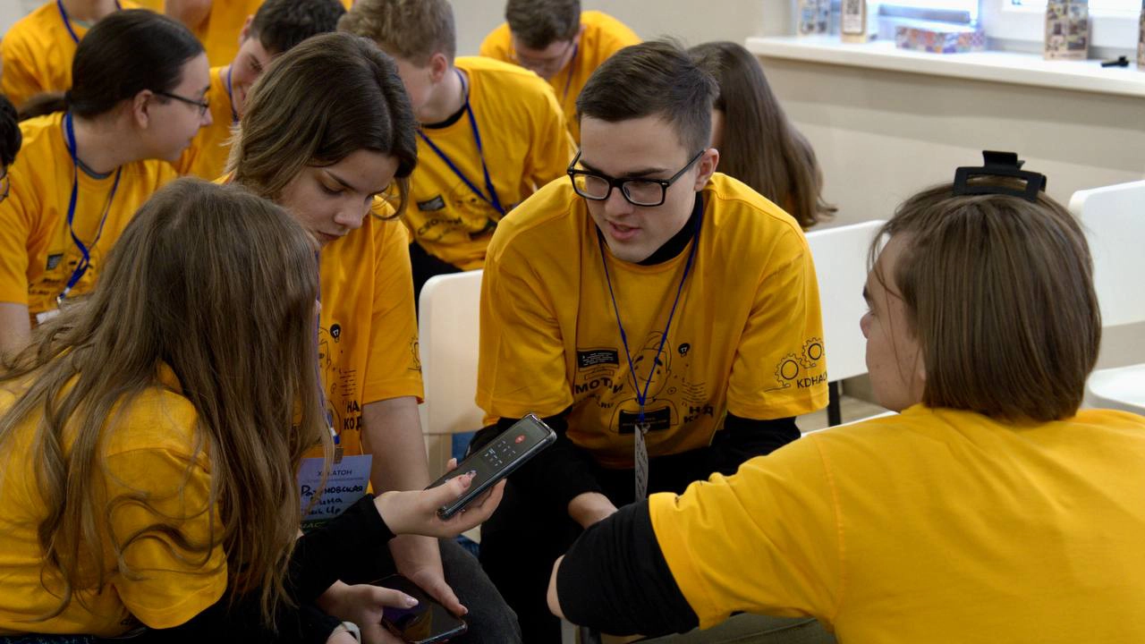 Na imagem, estudantes vestindo camisetas amarelas participam de uma dinâmica em grupo durante uma edição anterior do HackAtom Rosatom. O clima é de concentração e colaboração, refletindo o espírito do desafio internacional promovido pela Rosatom.