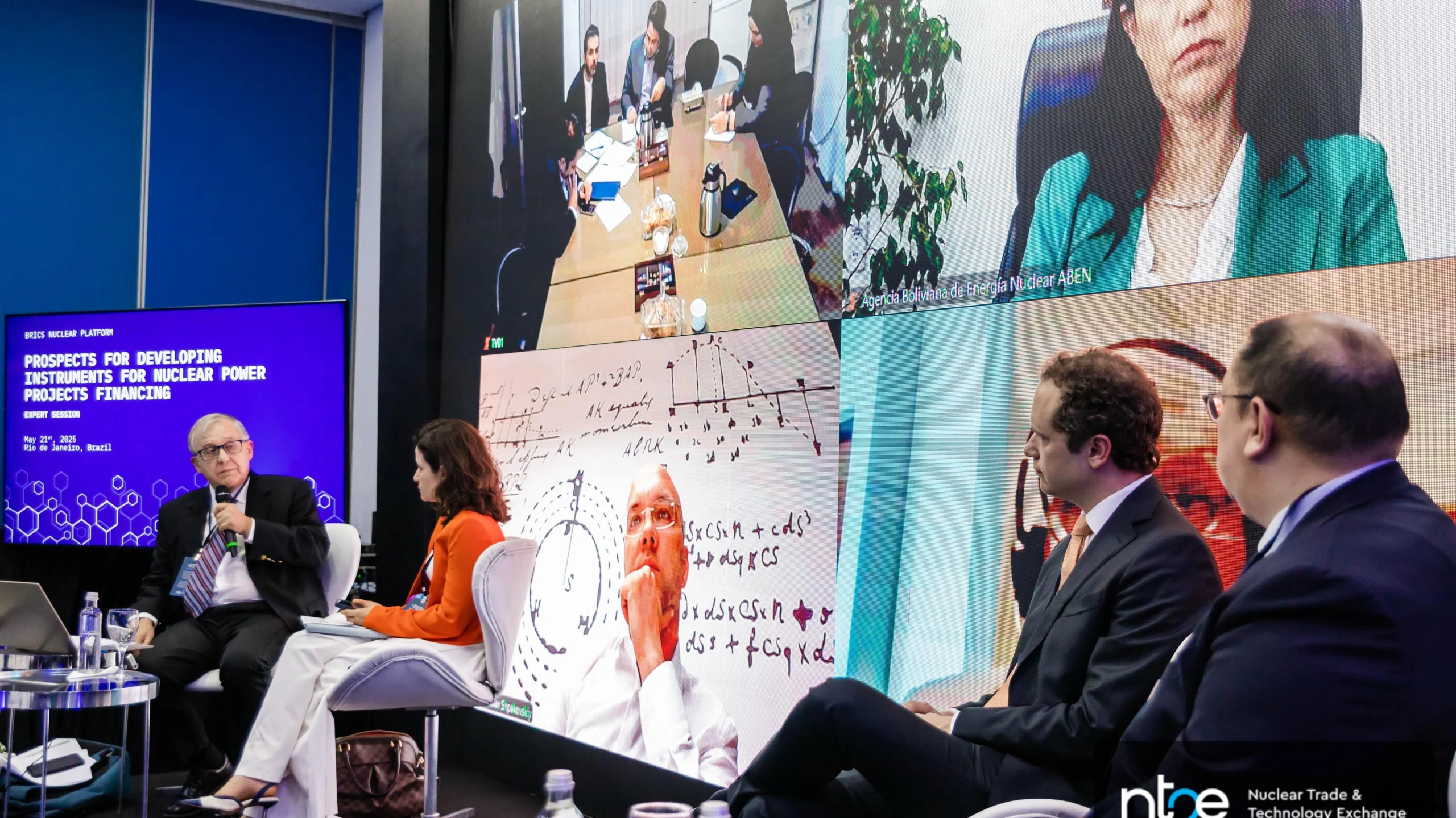 Especialistas participam de painel híbrido na NT2E 2025 sobre financiamento de projetos nucleares, promovido pela Plataforma Nuclear dos BRICS. Na tela, representantes internacionais contribuem por videoconferência, enquanto debatedores presenciais discutem modelos financeiros e inovação no setor.