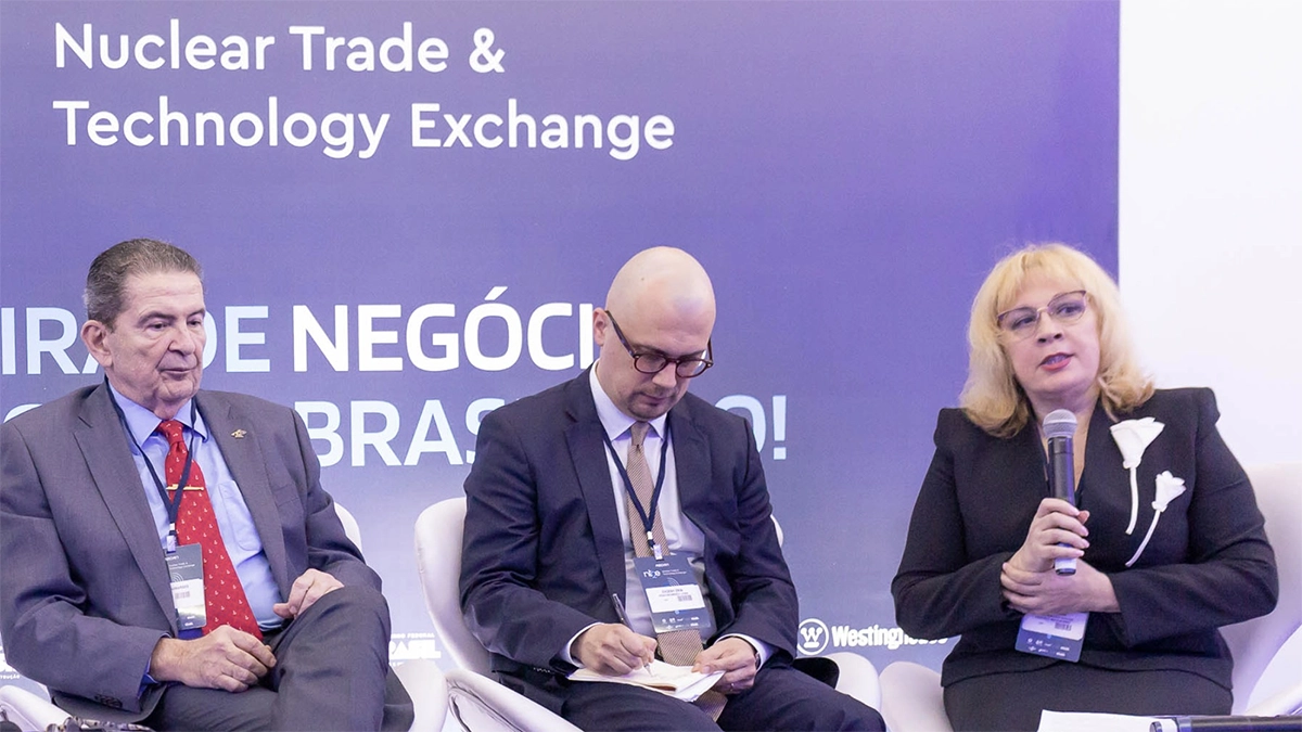 A vice-reitora do MEPhI, Elena Vesna, fala ao microfone durante painel da feira Nuclear Trade & Technology Exchange (NT2E), no Rio de Janeiro. Ao lado dela, dois participantes acompanham atentamente a discussão sobre o futuro da energia nuclear e a formação de novos profissionais para o setor.