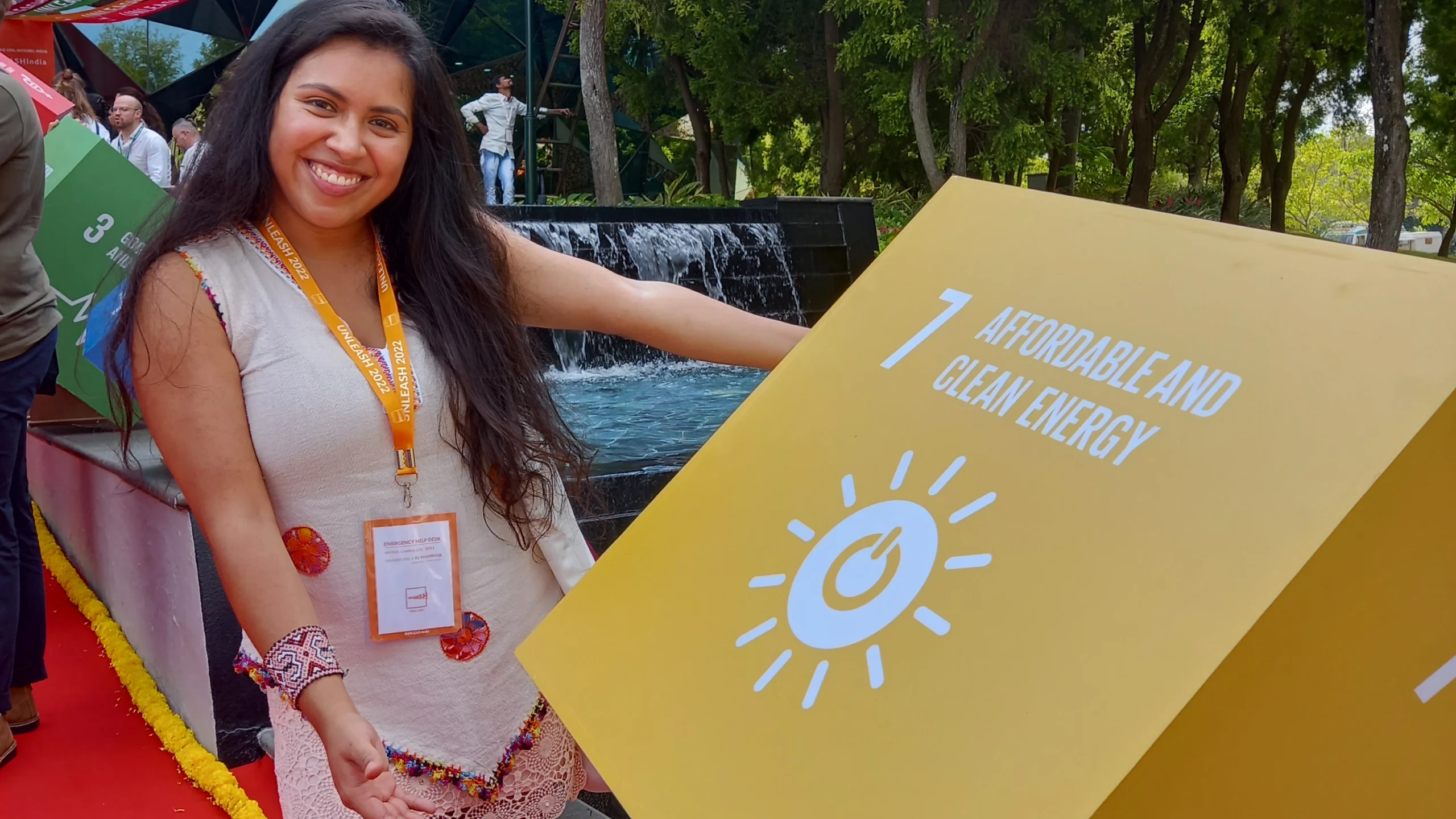 Joyce Mendes, ativista climática colombiana, sorri ao lado de um cubo amarelo que representa o Objetivo de Desenvolvimento Sustentável (ODS) 7, sobre energia limpa e acessível.