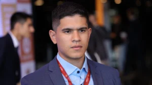 Osman Cesar Granada Galvis, jovem pesquisador latino-americano, veste blazer azul e crachá do BRICS Youth Energy Summit, olhando com expressão séria durante o evento.
