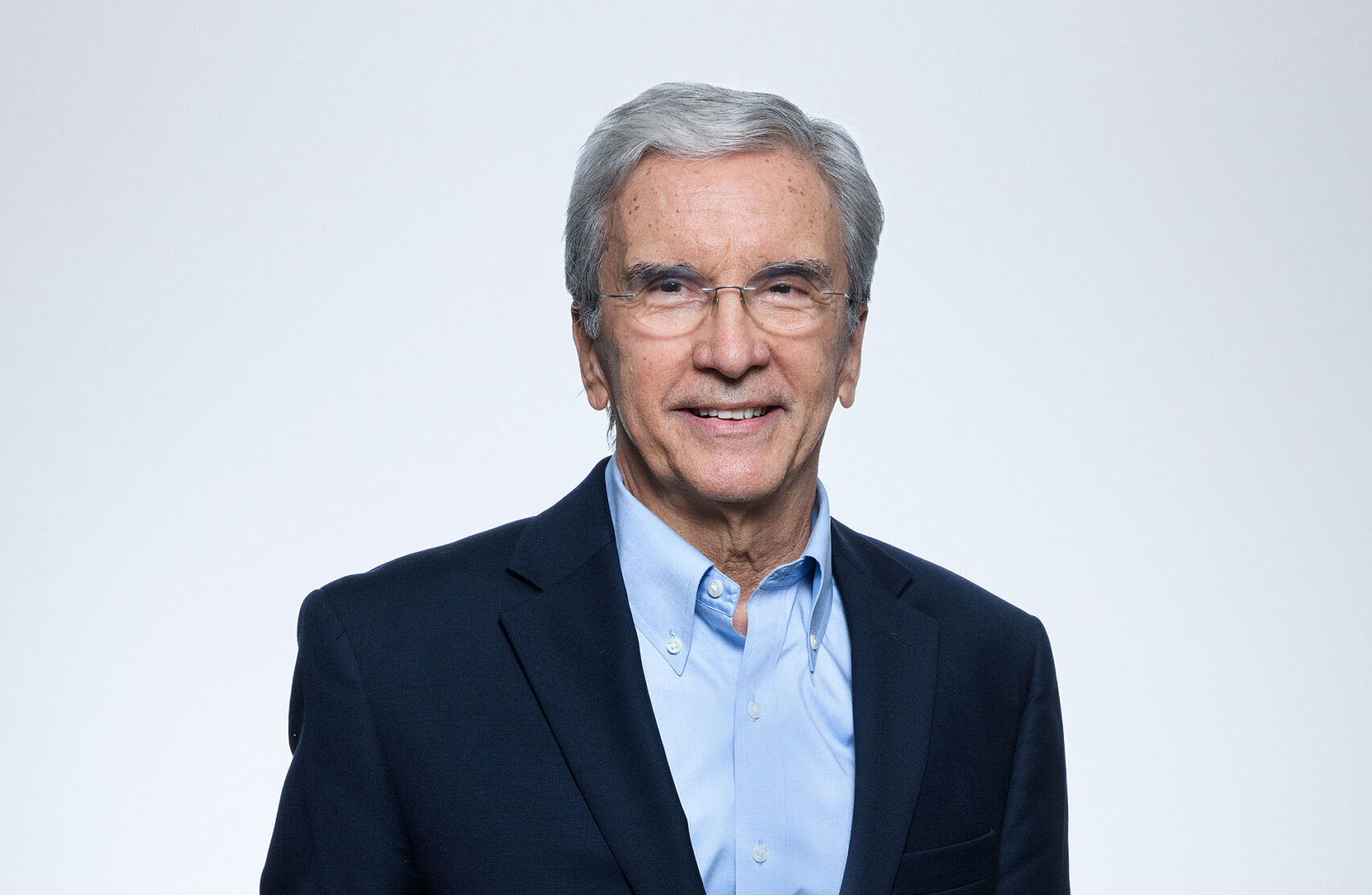 Retrato de homem de cabelos grisalhos, usando blazer azul-marinho e camisa azul clara, em fundo neutro, para ilustrar anúncio institucional de novo conselheiro em escritório de advocacia.