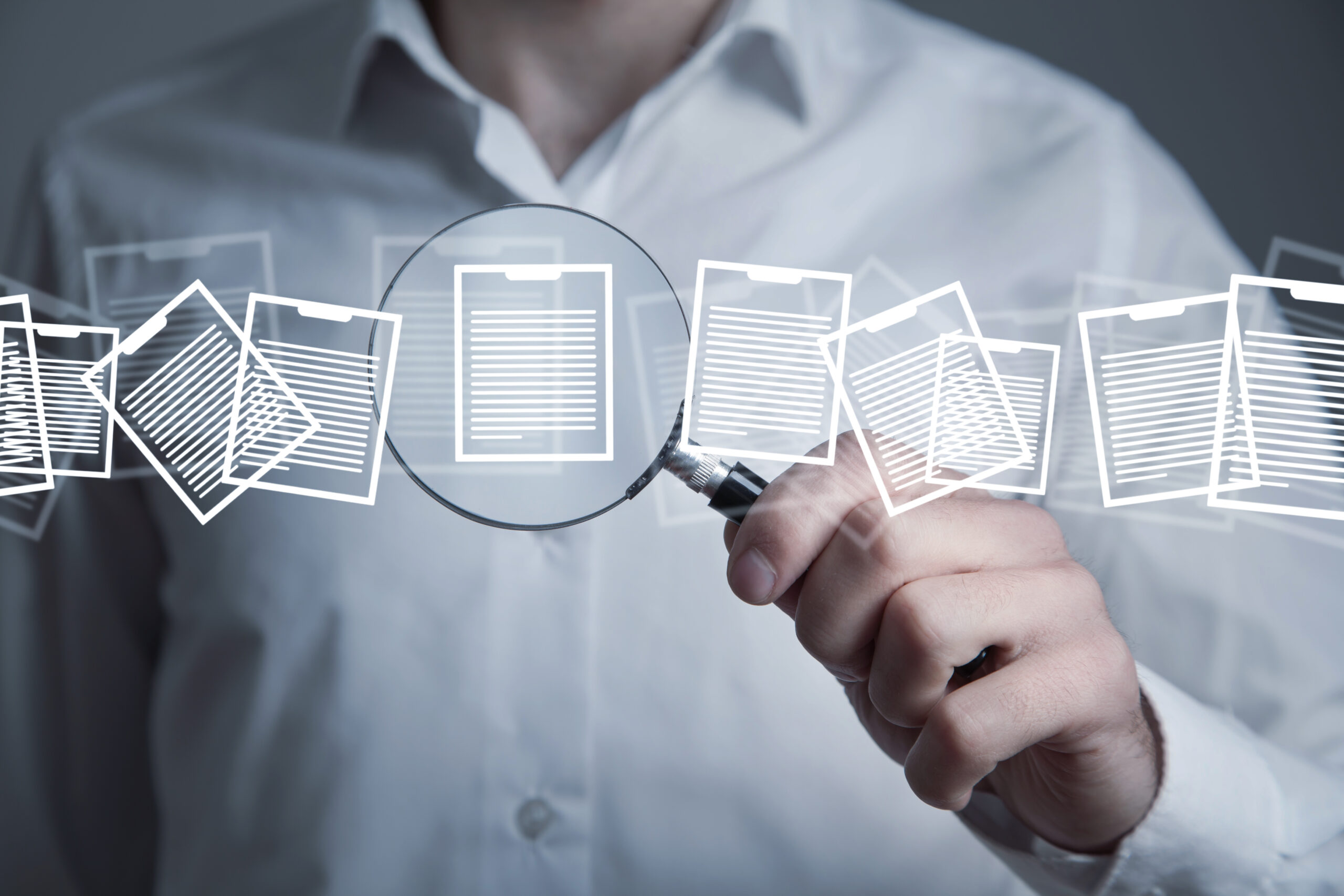 Pessoa usa lupa para analisar documentos digitais, representando gestão documental inteligente, busca de informações e governança de dados jurídicos com apoio de tecnologia