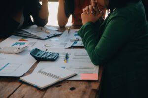 Empresária preocupada analisa relatórios financeiros e calculadoras sobre uma mesa, em cenário que representa endividamento e dificuldades de gestão.