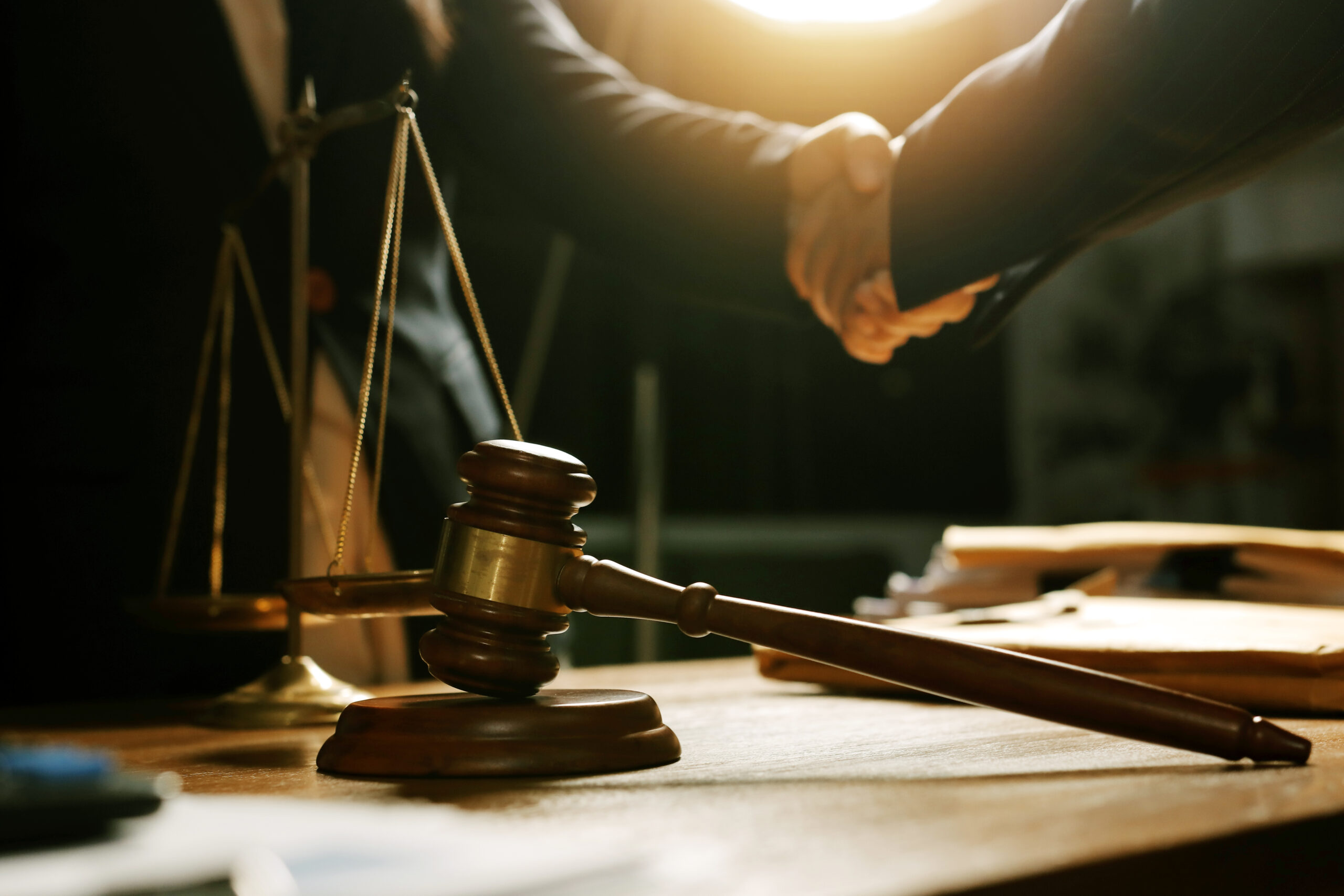 Martelo, balança da Justiça e aperto de mãos em escritório jurídico, representando negociação, recuperação judicial e acordos entre empresas e credores