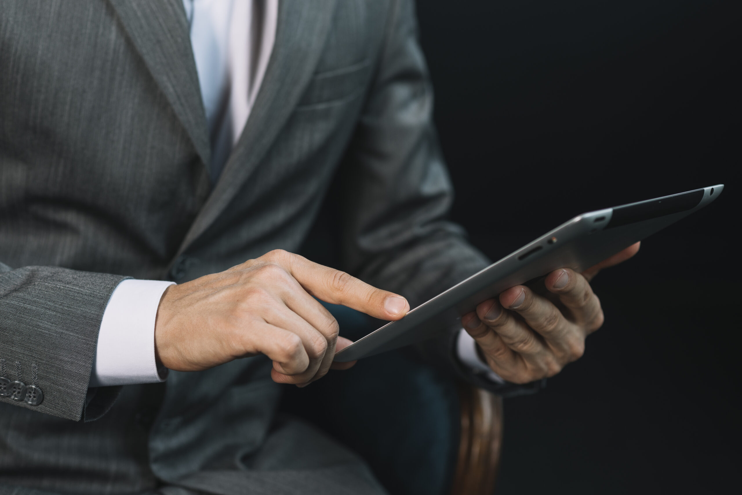 Profissional de terno utiliza tablet em ambiente corporativo, em imagem que representa tecnologia, digitalização e uso de ferramentas digitais no trabalho