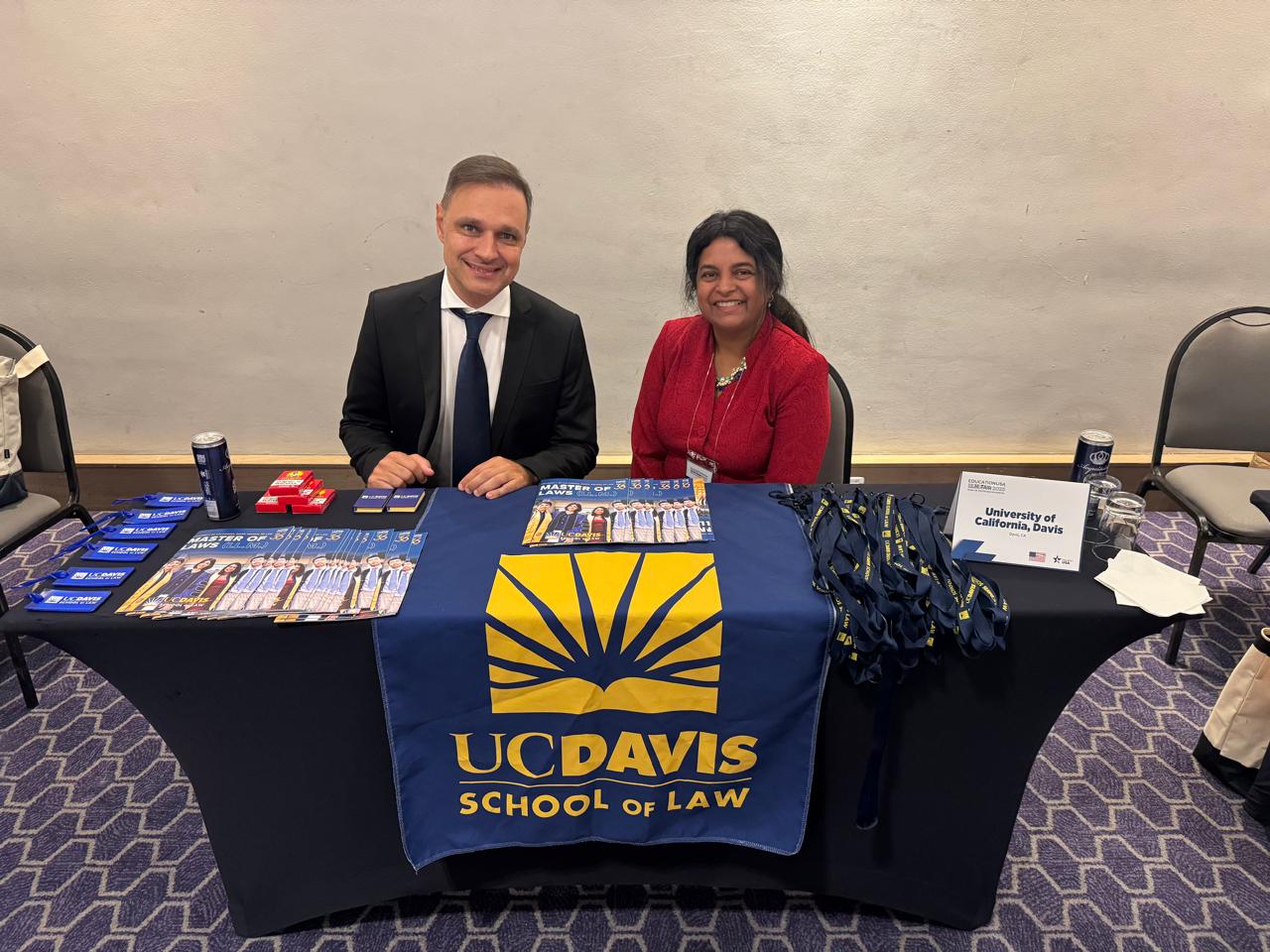 Representantes em estande da UC Davis School of Law durante evento de educação internacional, com materiais sobre programas jurídicos da universidade