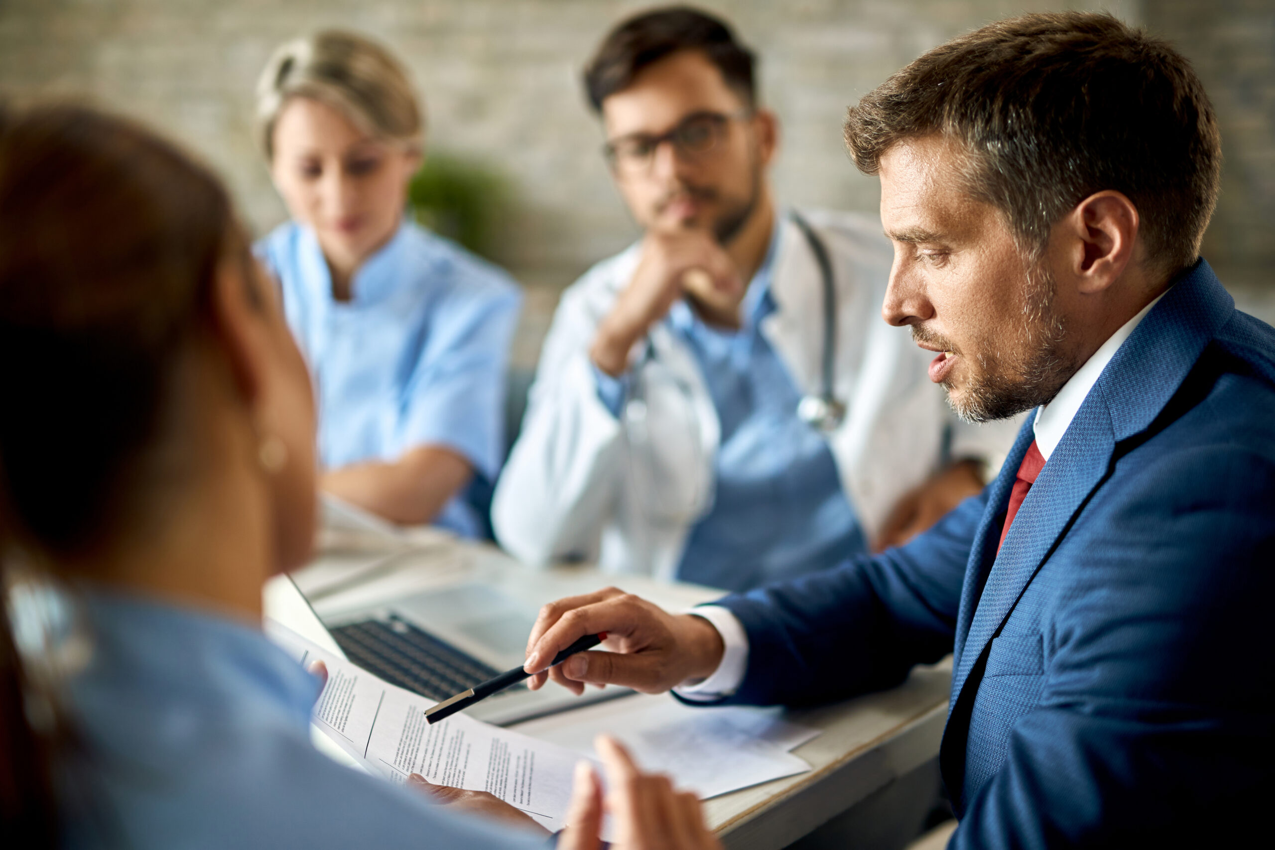 Advogado analisa documentos em reunião com profissionais de saúde, em imagem que representa orientação jurídica relacionada a direitos de pacientes e benefícios após tratamento médico