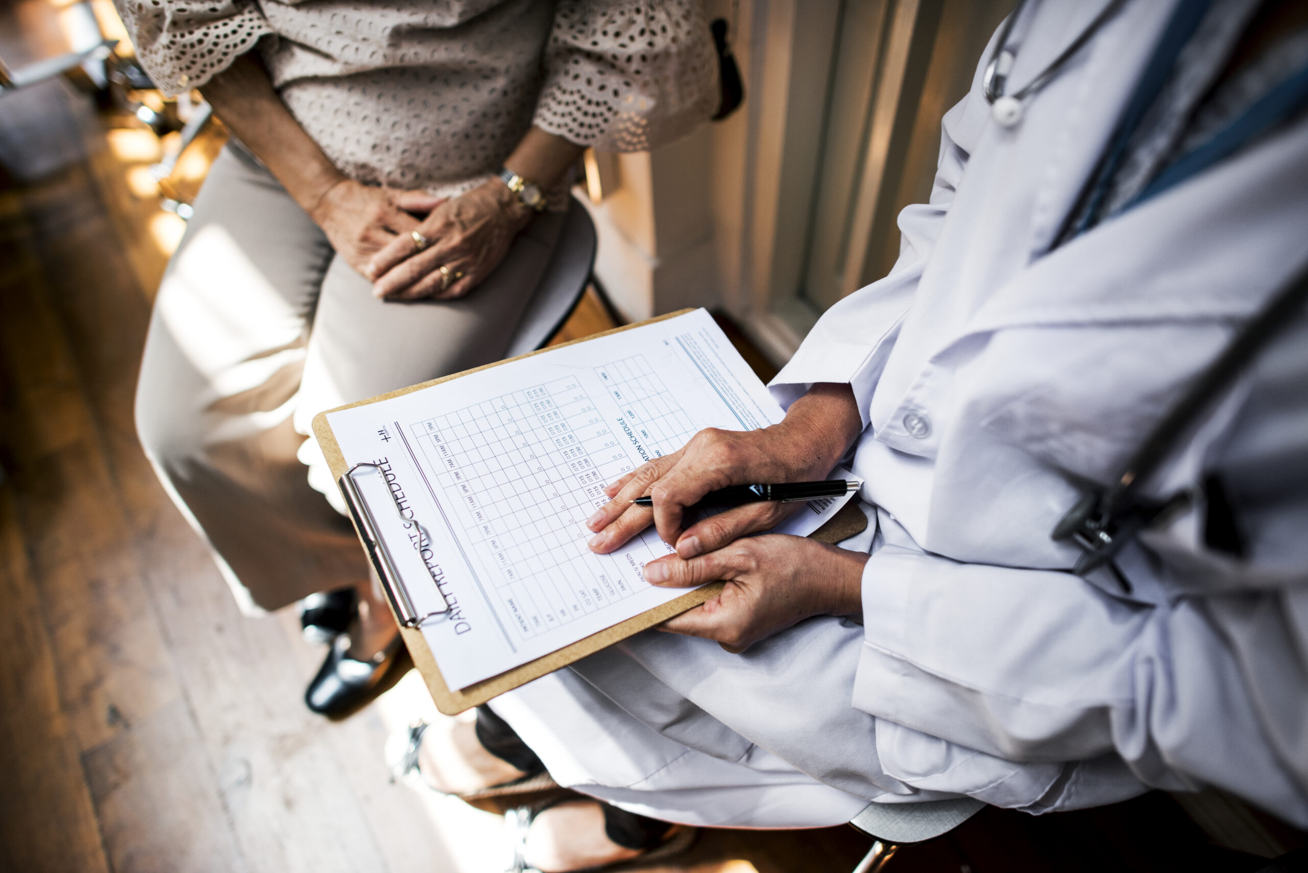 Paciente conversa com médica durante consulta, enquanto a profissional analisa documentação clínica e registros de saúde